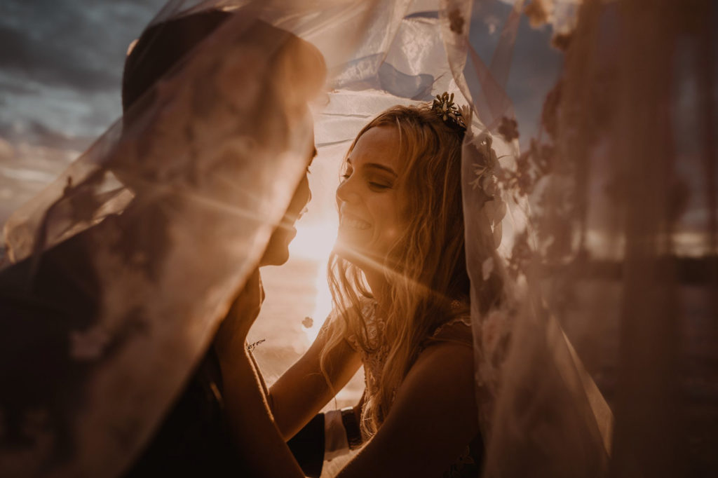 A couple is leaning in for a kiss after they get married in Vanuatu, with the sun setting behind them.