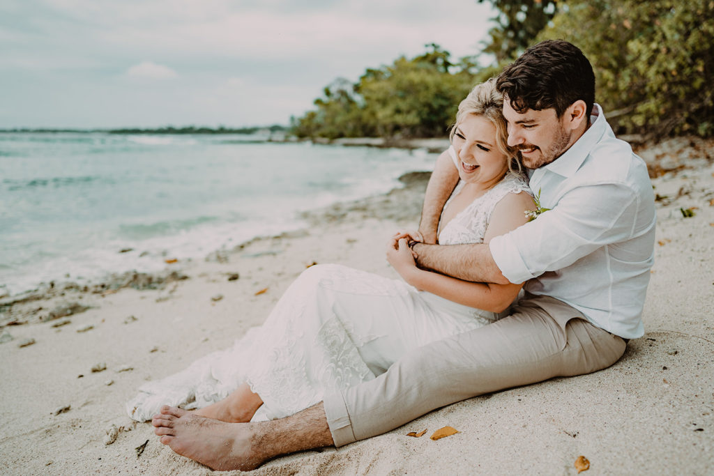 Newlyweds couple sitting on the beach and laughing after their wedding ceremony on Erakor Island