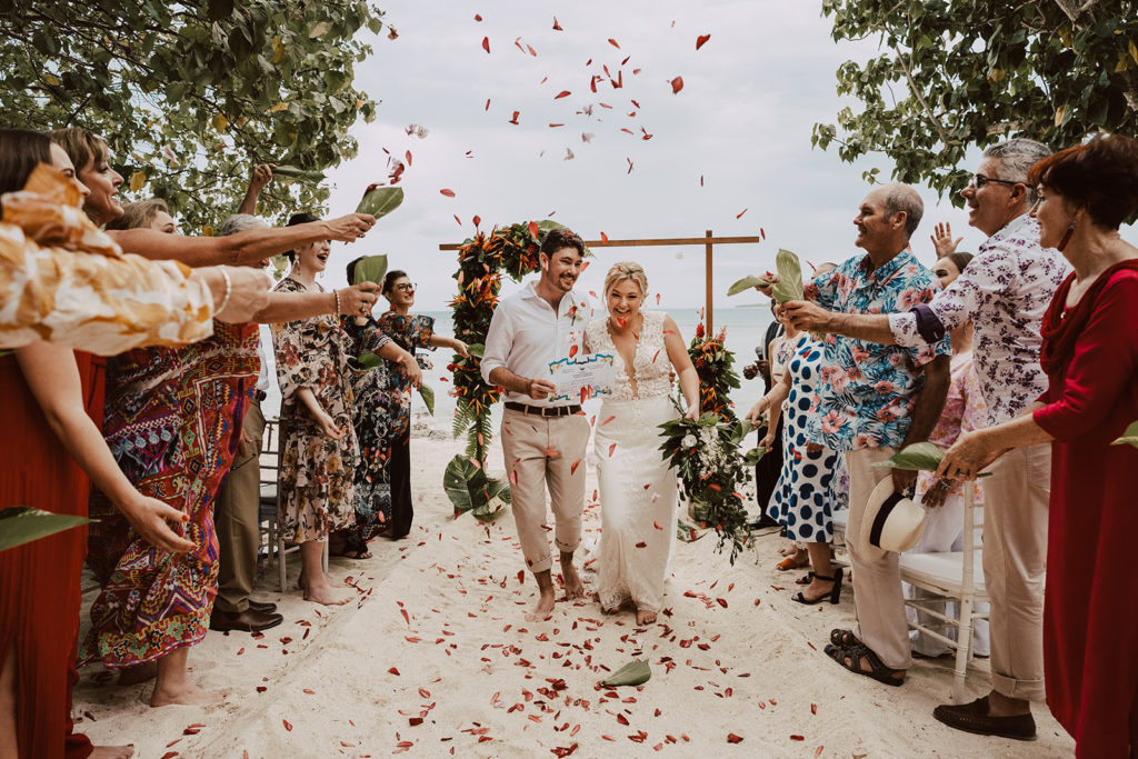 A couple exiting their wedding ceremony at sunset beach on Erakor Island under a shower of flower petals