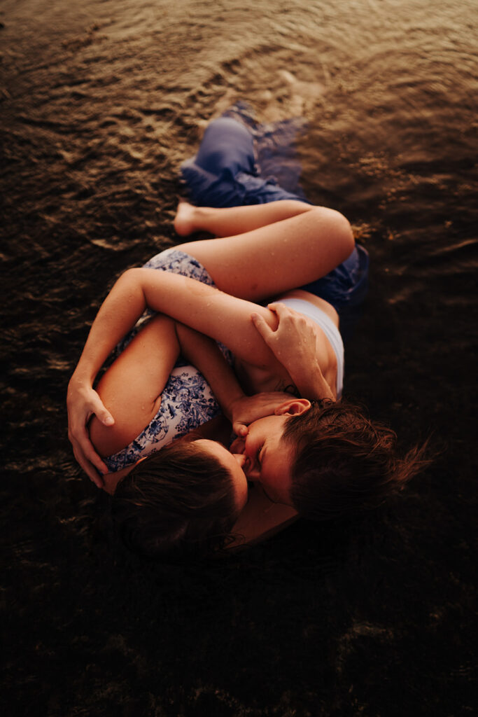 LGBTQ couple hugging on a beach covered by tide water in the sunset light during their pre-wedding photoshoot